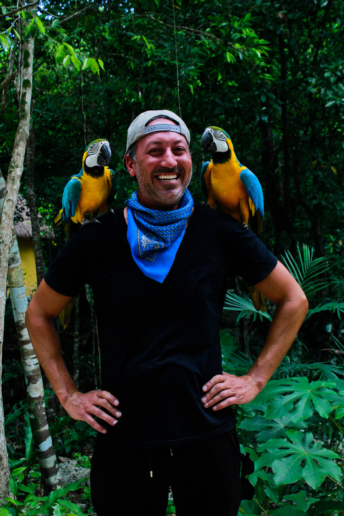 Yaniv Frantz, former SureTrader senior sales manager, photographed outdoors with two blue-and-gold macaws on his shoulders